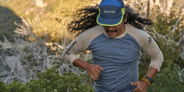 Runner with long curly hair in a blue Fractel seasonal trucker hat with neon yellow trim and a raglan long sleeve top