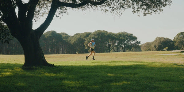 Runner in a light blue singlet and cap running through a sunlit park, Velocity 4 running collection