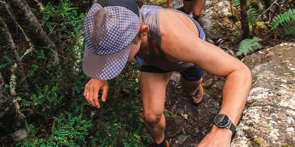 Trail runner scrambling over rocks in a Fractel fitted race day cap with a lilac dotted print