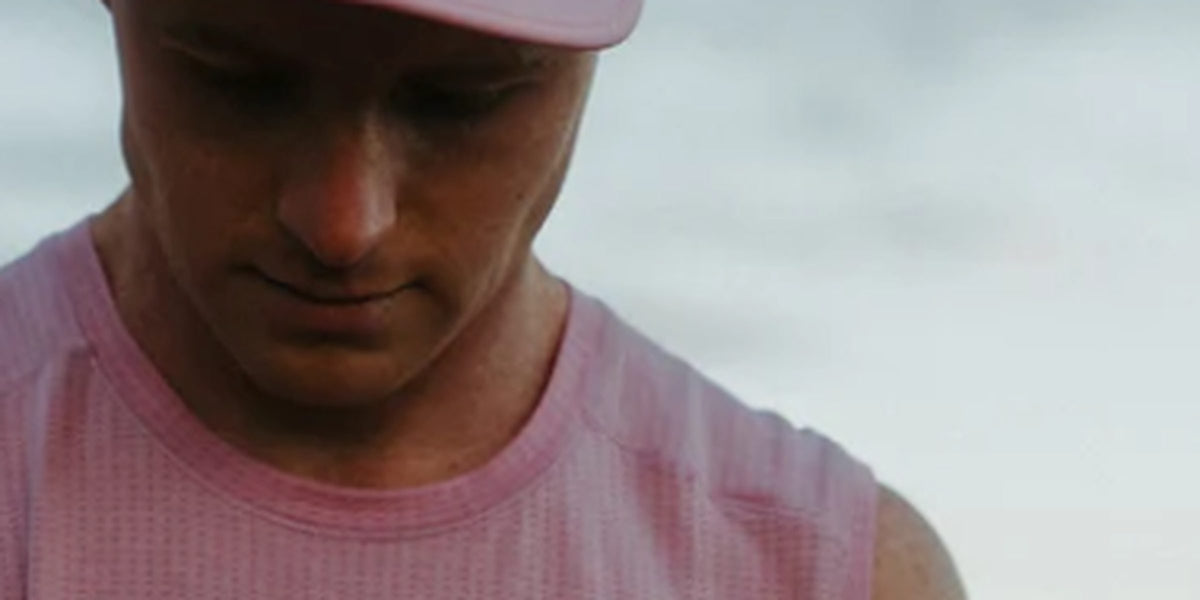 Runner in a pink Fractel singlet and cap looking down, featured in our gifts for runners collection