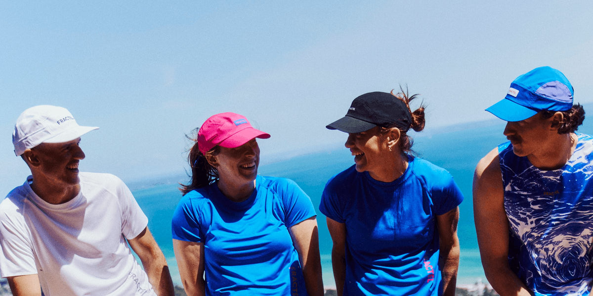 Four runners laughing together in white, pink, black and blue Fractel running caps by the sea