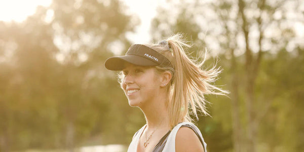 Smiling runner in a black Fractel running visor with her ponytail blowing in golden light