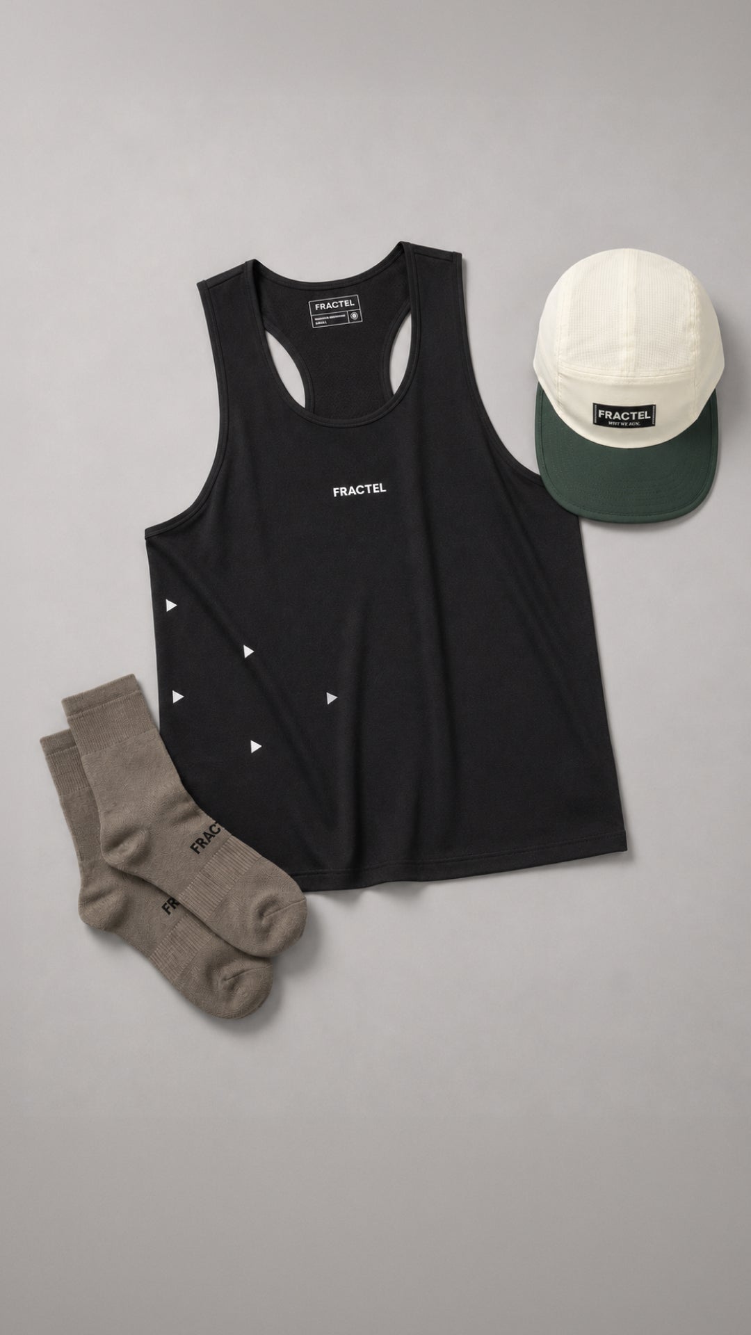 A black athletic tank top with a white Fractel logo on the chest, styled in a flat lay with a white and green running cap and a pair of socks on a solid gray background.